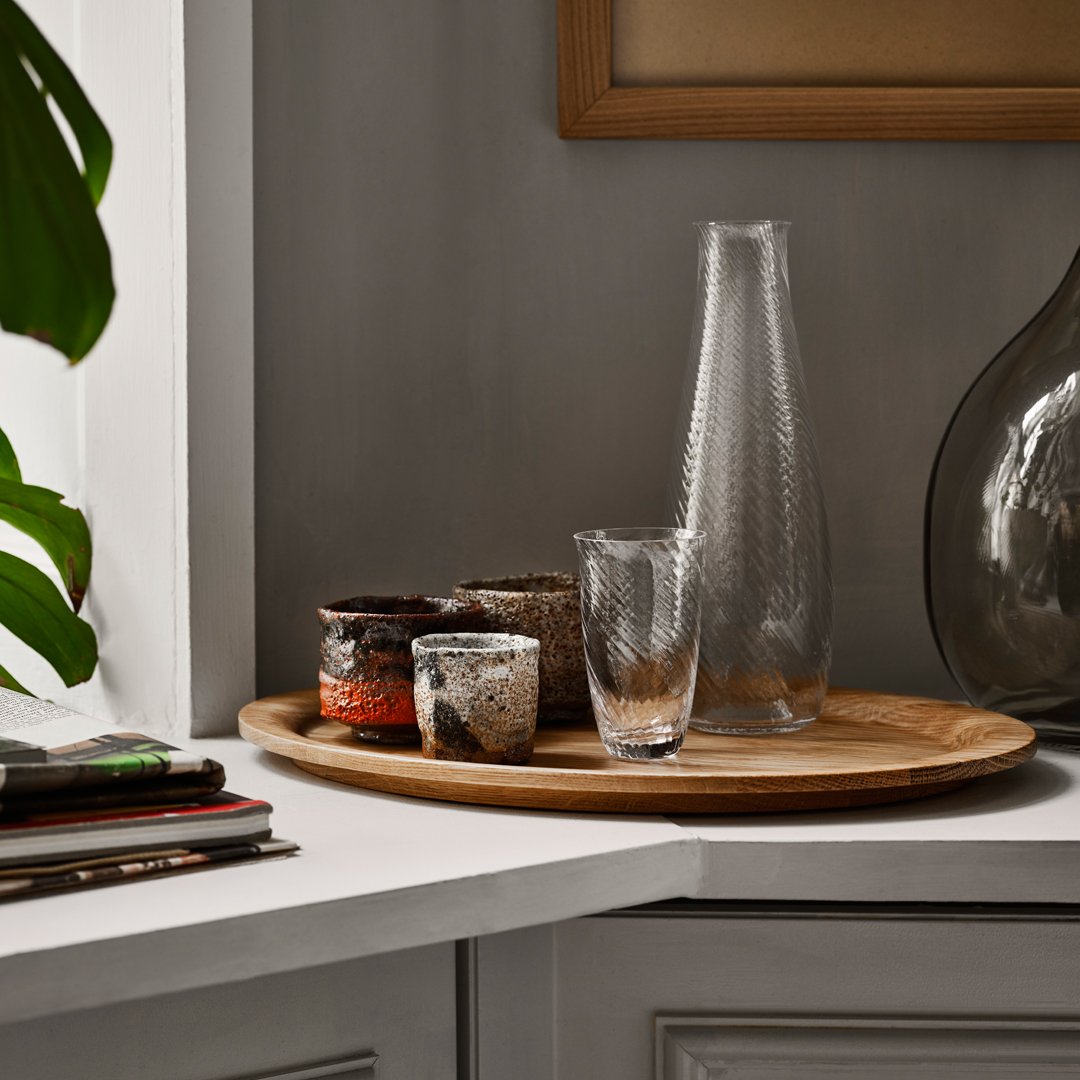 "Textured glass carafe and cups on a wooden tray, featuring earthy tones and subtle patterns."