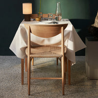 Elegant cream tablecloth drapes over a wooden table, complemented by natural wood tones and a textured woven chair.