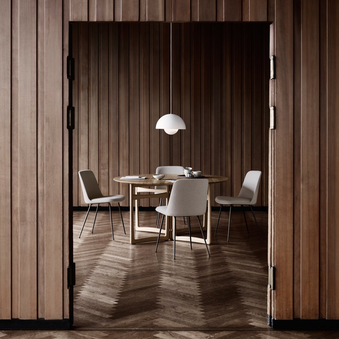 Elegant wooden interior featuring herringbone flooring, soft gray chairs, and a simple white pendant light.