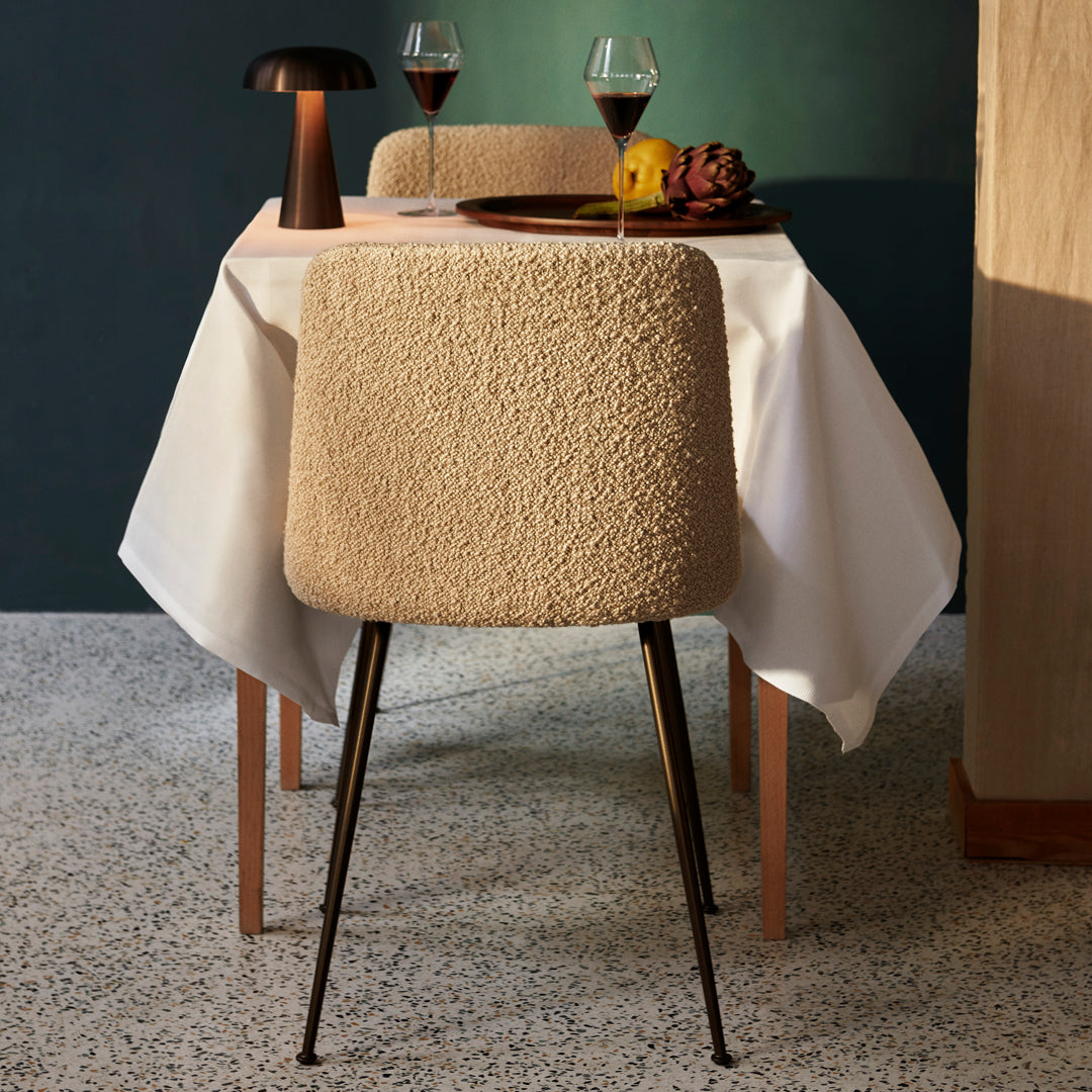 Stylish beige textured chair with black legs, paired with a white tablecloth in a sophisticated dining setting.