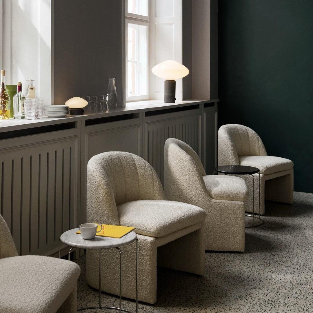 Textured cream chairs with curved backs, paired with a marble table and dark green wall accents. Cozy and modern design.