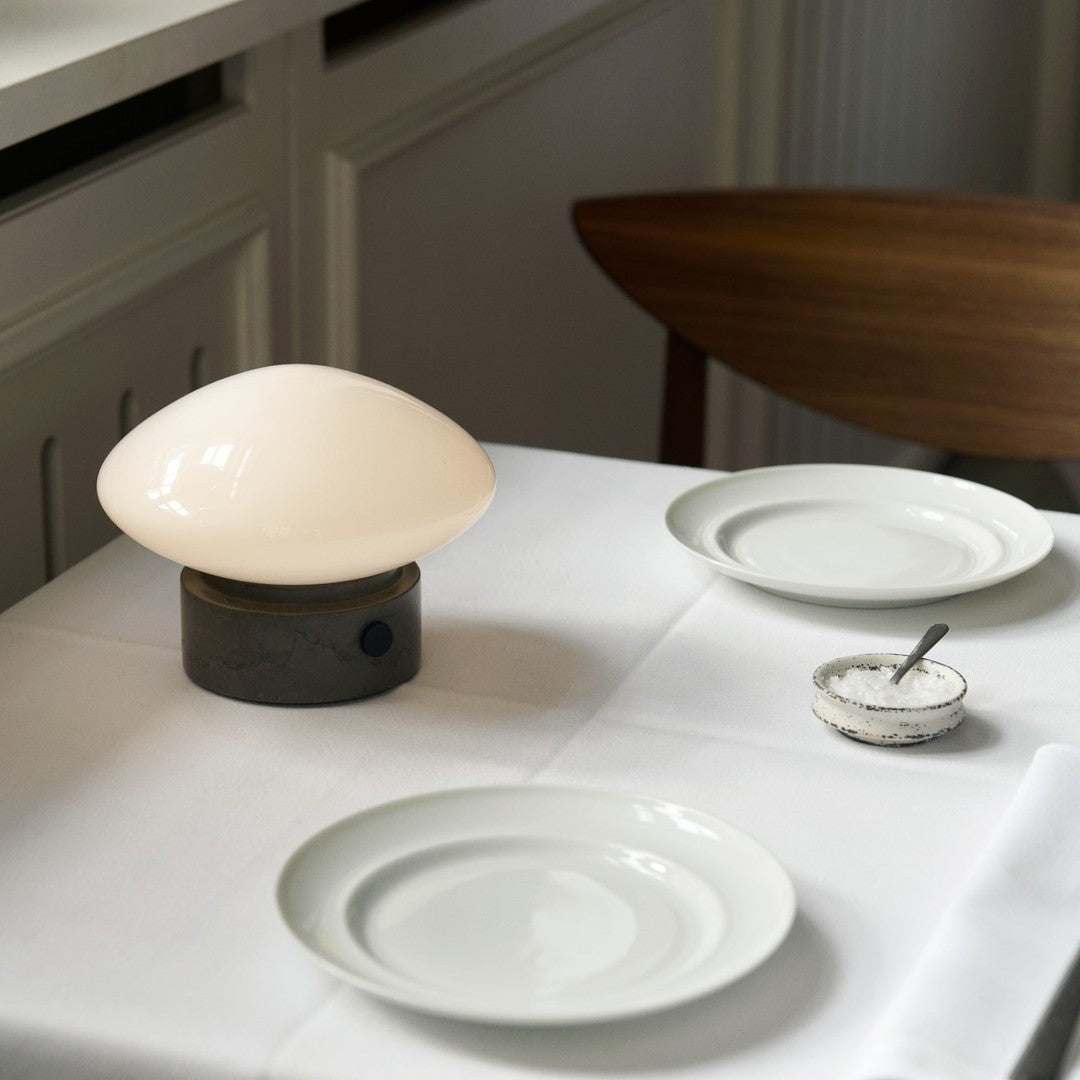 Cream-colored lamp with an oval shape on a dark gray base, set against a white tablecloth with white plates.
