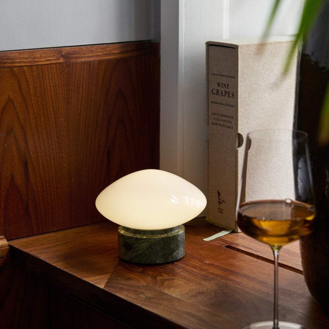Soft white glass lamp with a green marble base, set against rich wooden tones and natural textures.