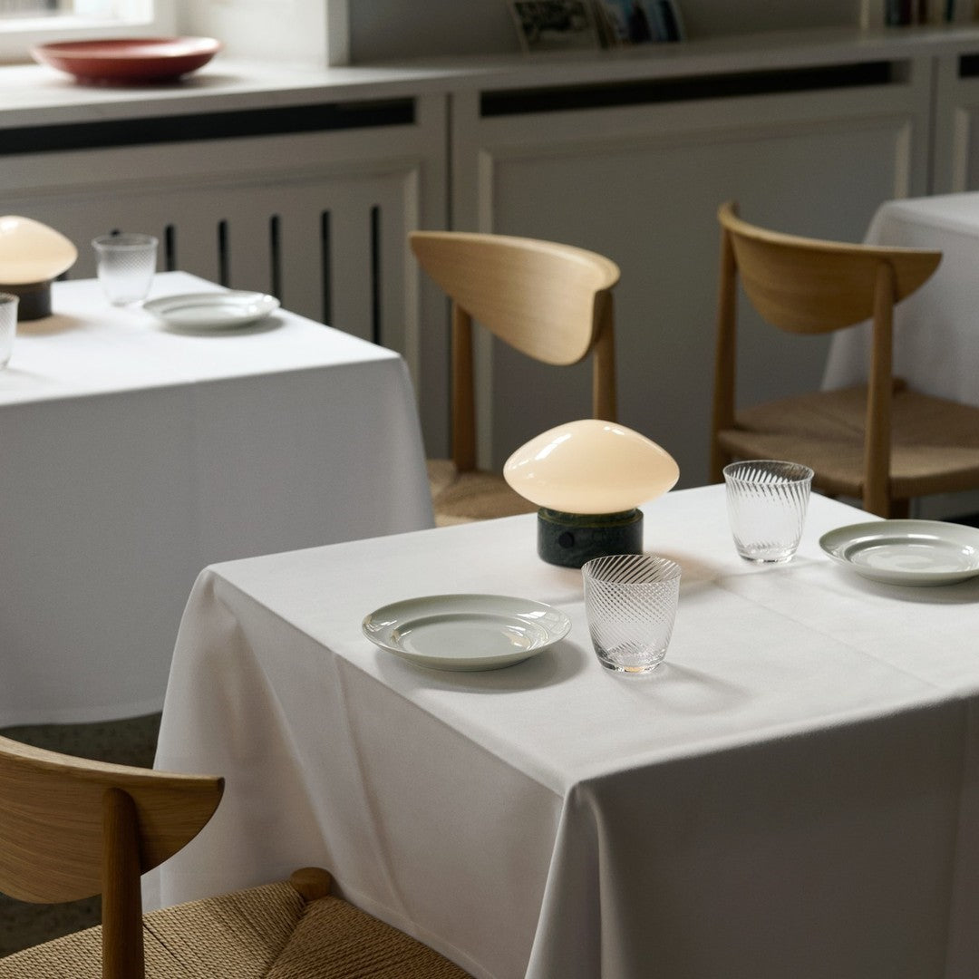 Elegant white tablecloths with soft green plates and patterned glassware, complemented by warm beige lighting.