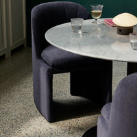 Dark blue upholstered chair beside a round marble table; speckled floor adds texture and visual interest.