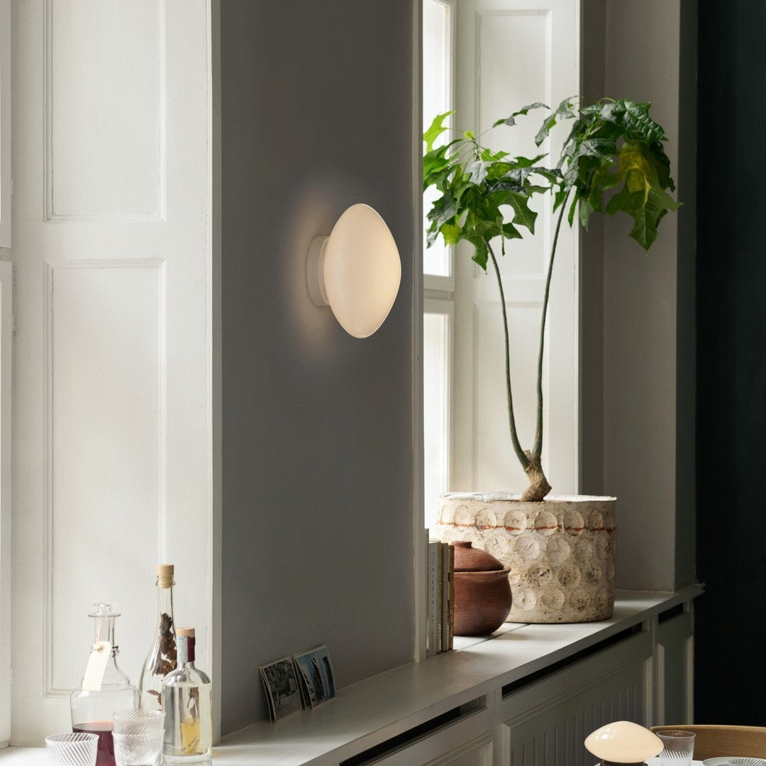 Modern beige wall lamp on gray wall, with green plant and natural textures for a calming aesthetic.