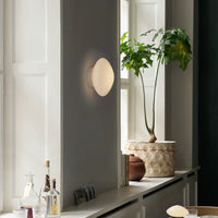 Modern beige wall lamp on gray wall, with green plant and natural textures for a calming aesthetic.