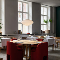 Modern dining space featuring red upholstered chairs, white table linens, and natural wood accents in a neutral-toned setting.