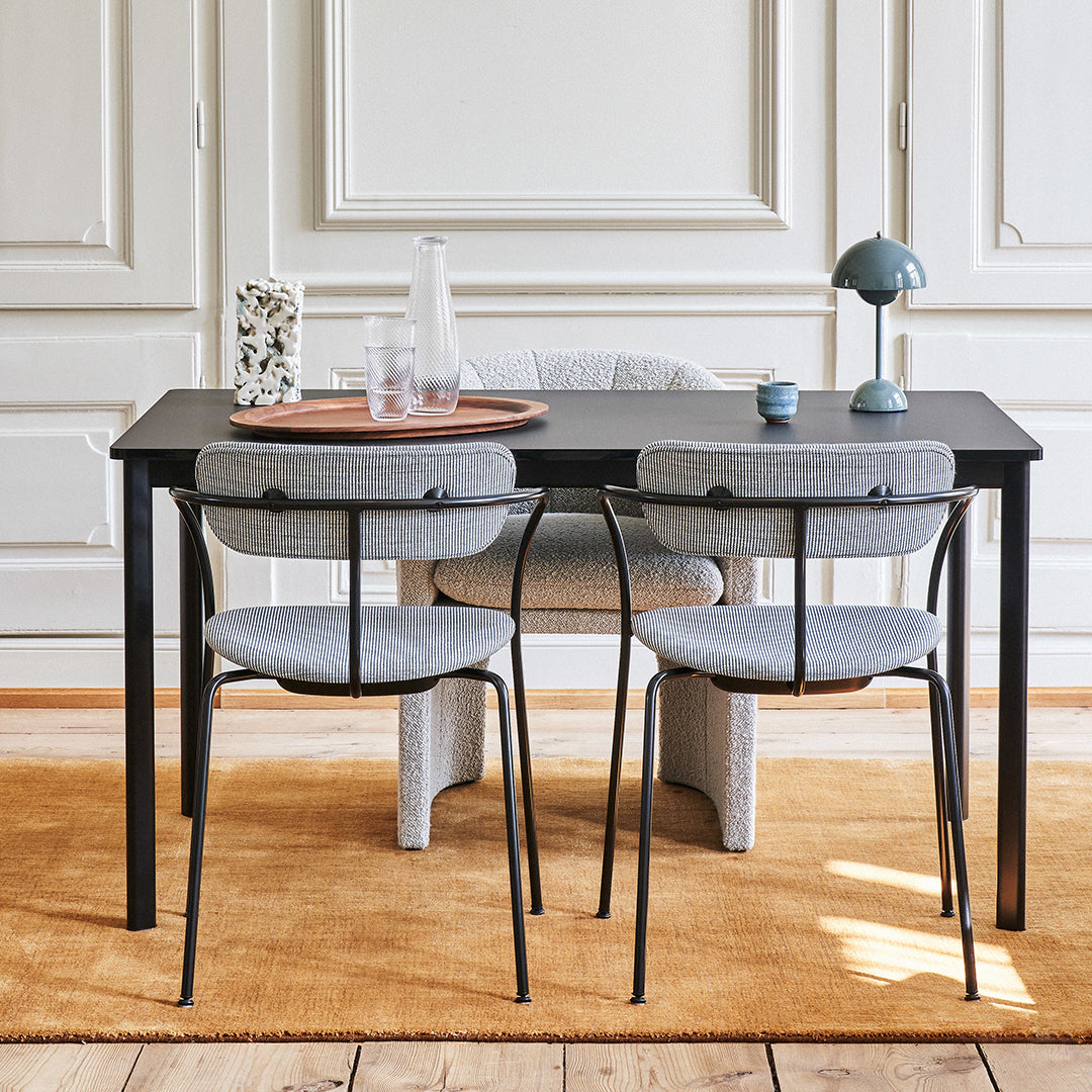 Gray upholstered chairs paired with a sleek black table on a warm, textured golden rug. Elegant minimalist design.
