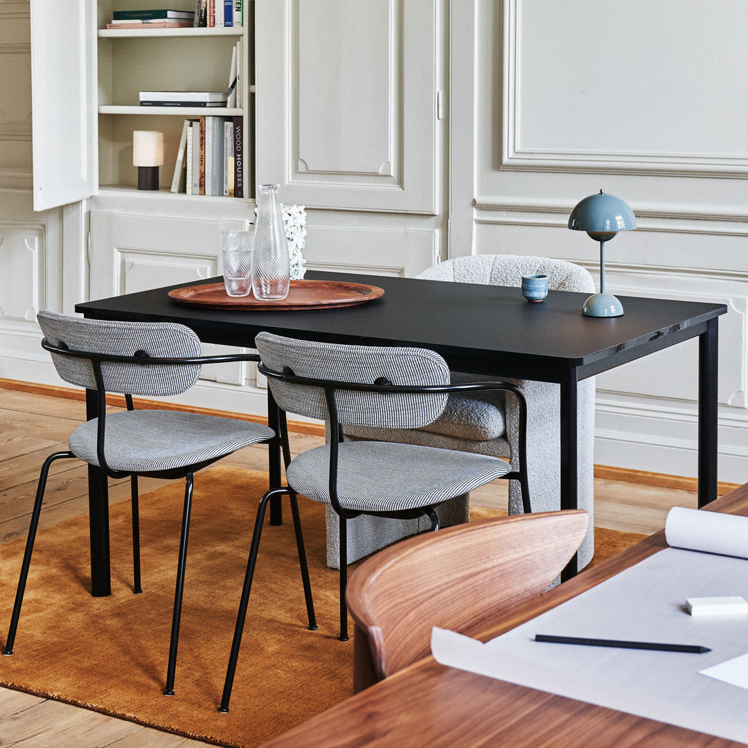 Modern black dining table with gray upholstered chairs, set against a warm orange rug in a bright, elegant room.