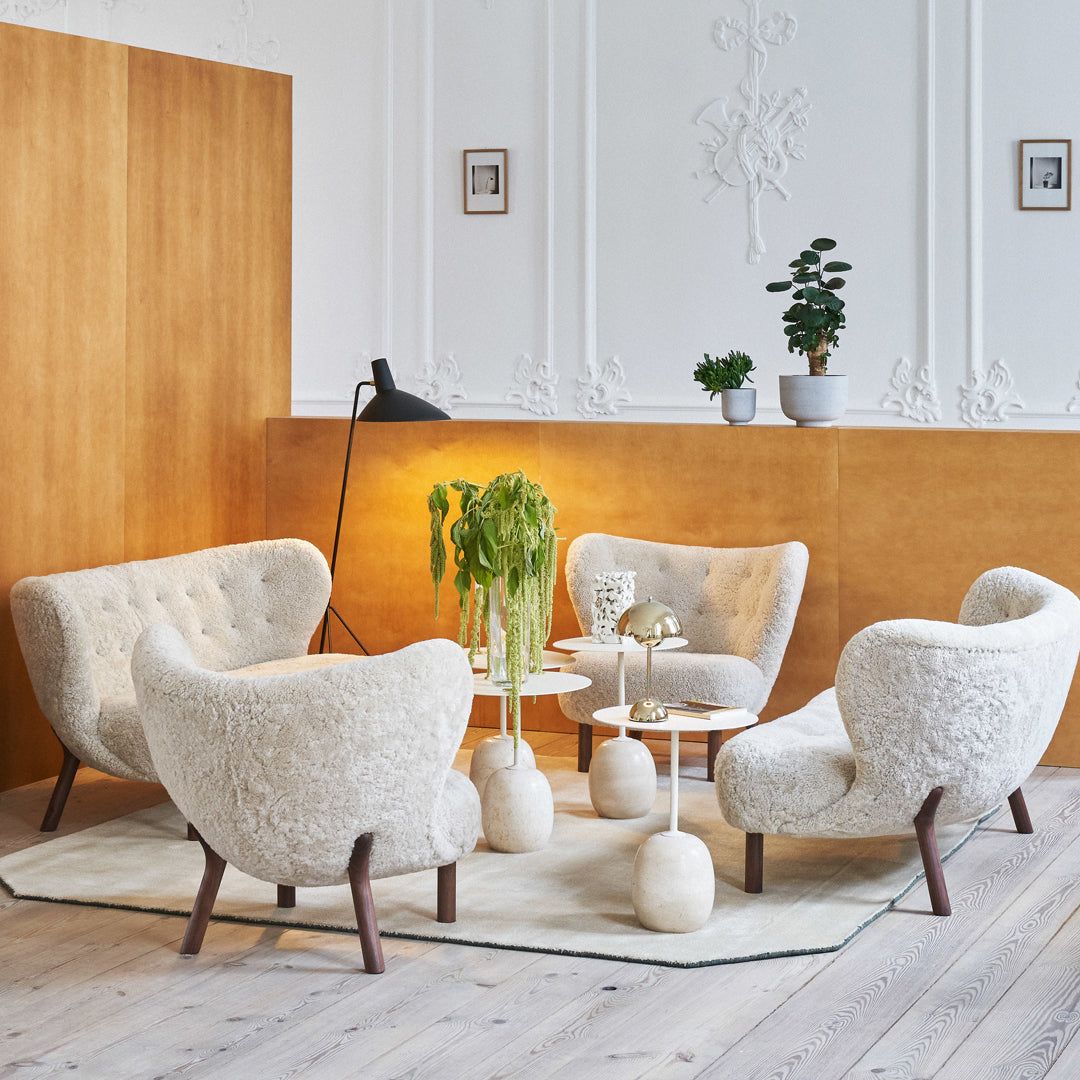 Cream-colored, textured armchairs with wooden legs, set against a warm wooden backdrop and elegant greenery.