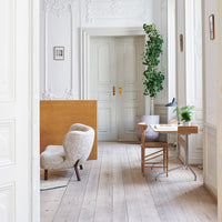 Cozy room with light wood floors, soft beige furniture, green plants, and white walls featuring decorative patterns.