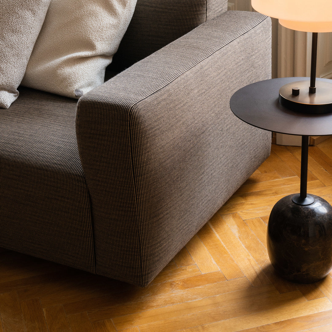 Taupe fabric sofa with textured pattern, paired with a sleek black side table on warm wood flooring.
