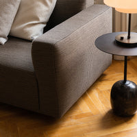 Taupe fabric sofa with textured pattern, paired with a sleek black side table on warm wood flooring.