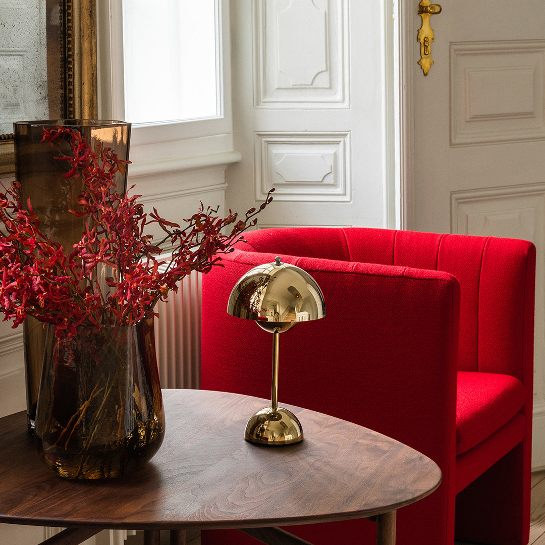 Red striped chair with a gold lamp and dark vase, complemented by vibrant red floral accents on a wooden table.