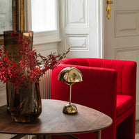 Red striped chair with a gold lamp and dark vase, complemented by vibrant red floral accents on a wooden table.