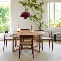 Round wooden dining table with dark brown chairs, featuring striped seat patterns, and a purple pendant light overhead.