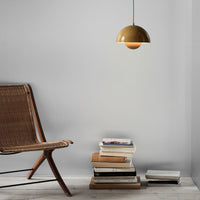 Gold dome pendant light hanging over a stack of books on a neutral-toned floor with a wooden chair.