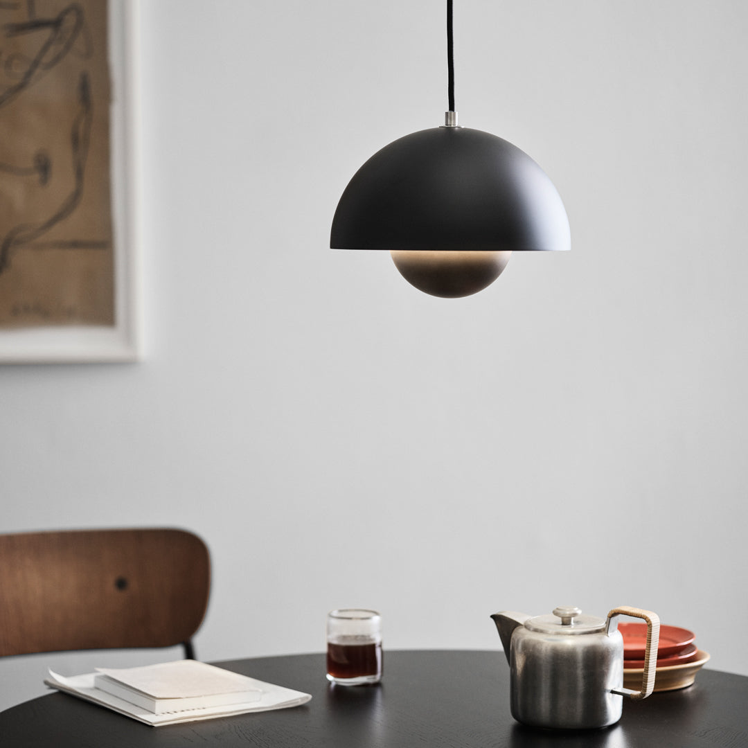 Modern black pendant lamp with a wooden accent, illuminating a stylish dining setting with warm tones.