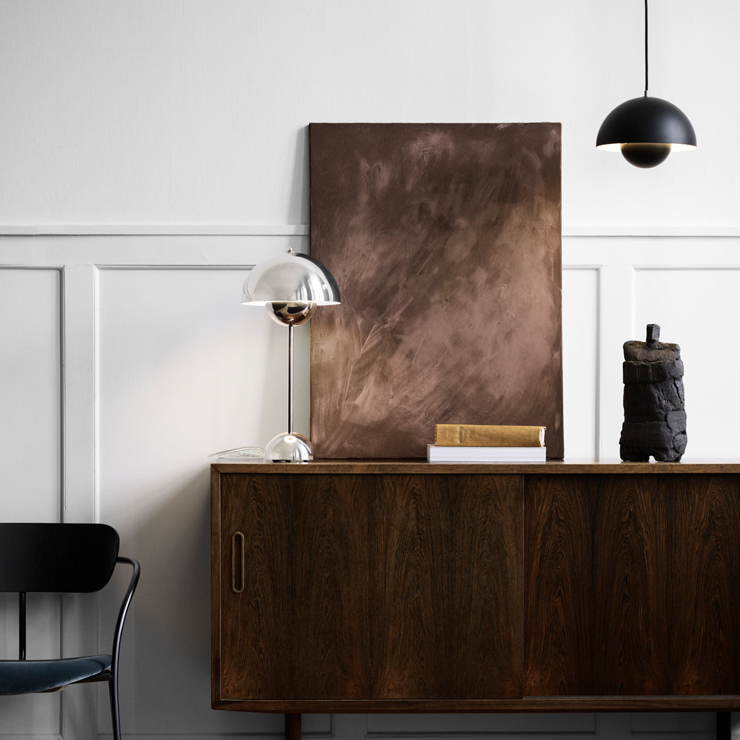 Abstract brown painting with soft gradients above a wooden sideboard, complemented by black and metallic decor elements.