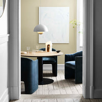 Elegant blue velvet chairs around a round wooden table, set against soft beige walls and a light abstract artwork.