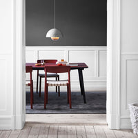 "Modern dining room featuring a red table, black legs, wooden chairs, gray walls, and a sleek pendant light."