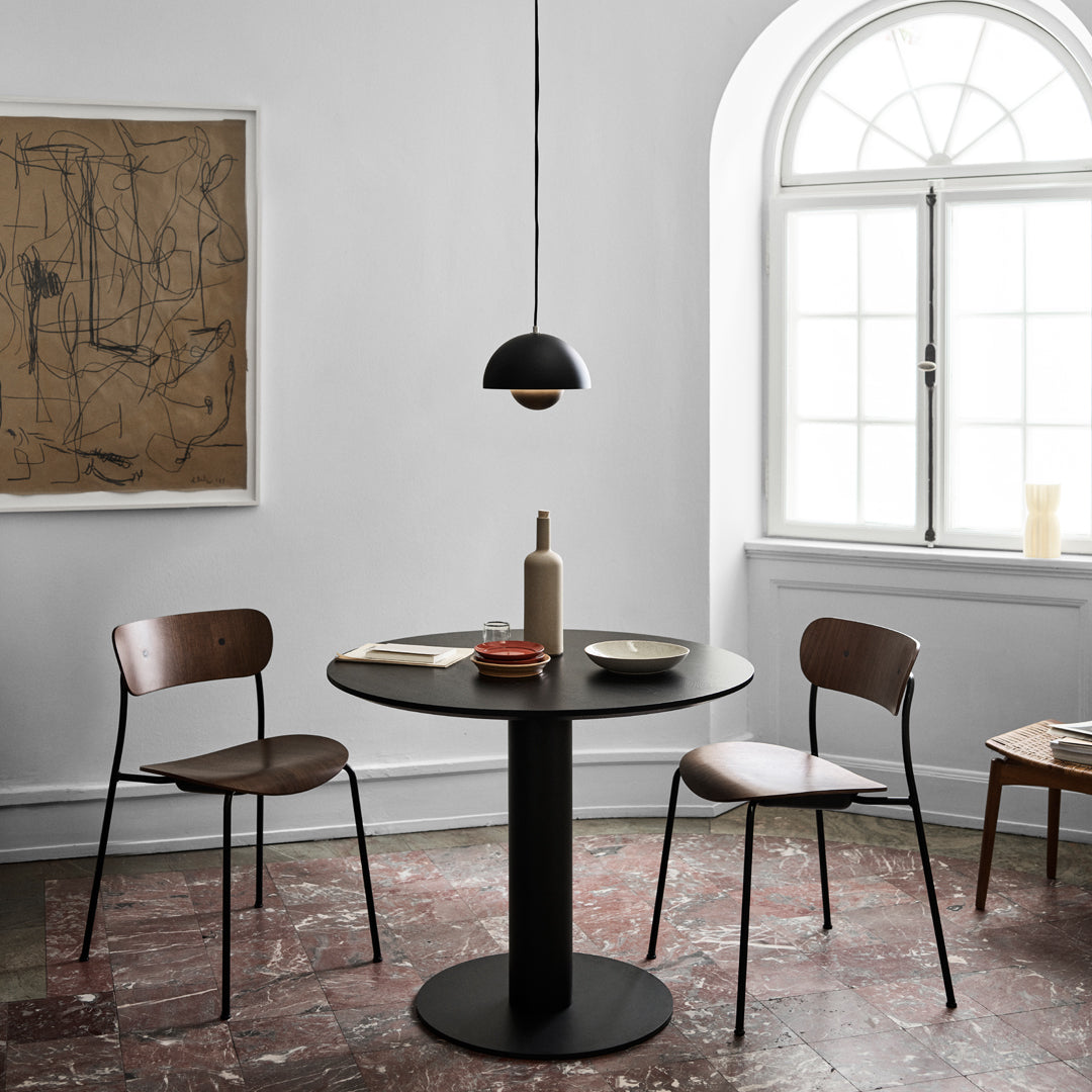 Modern black table with wooden chairs, set against a neutral backdrop and textured brown floor, accented by minimalist decor.