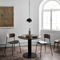 Modern black table with wooden chairs, set against a neutral backdrop and textured brown floor, accented by minimalist decor.