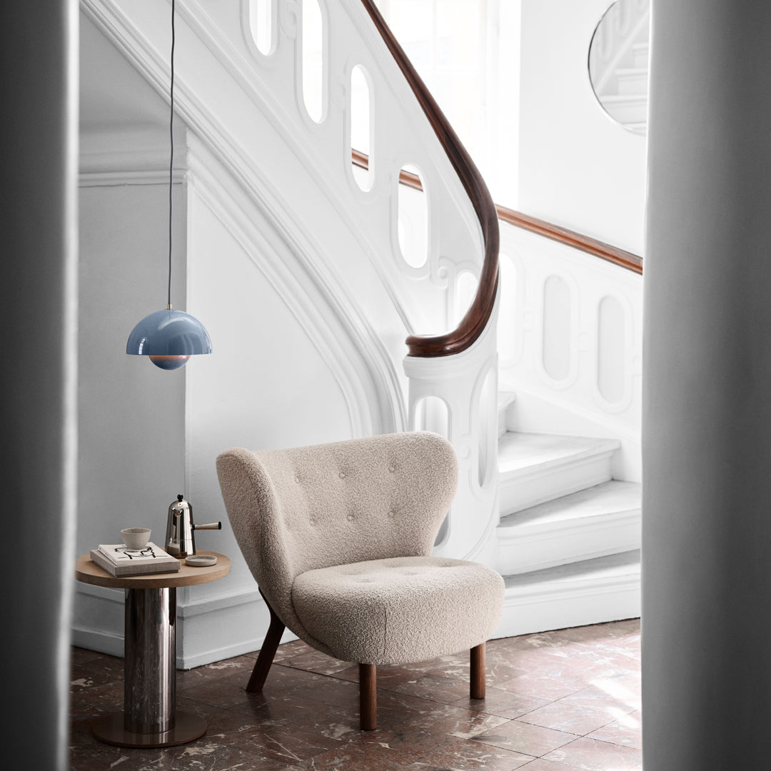 Cream tufted chair with wooden legs, set against a white staircase and gray accent table, featuring soft blue pendant light.