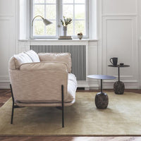 Beige textured sofa on a muted yellow rug, featuring black accent tables in a bright, airy room.