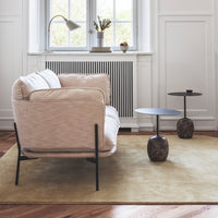 Beige sofa with textured fabric, black metal legs, and round side tables; soft yellow rug and neutral walls enhance the palette.