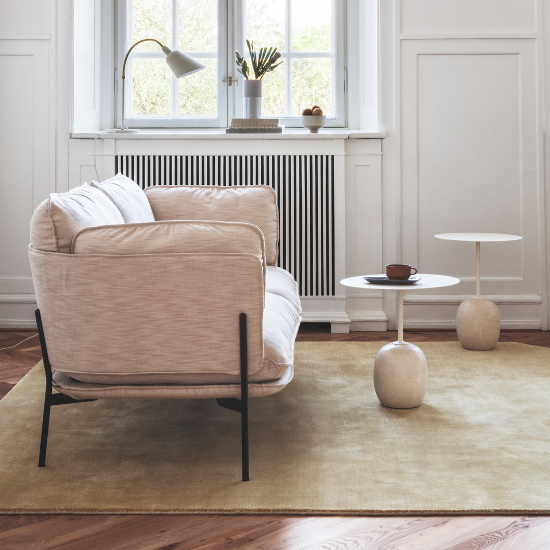Soft beige armchair with white cushions on a light yellow rug, featuring minimalist black legs and round clay side tables.