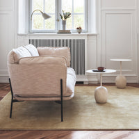 Soft beige armchair with white cushions on a light yellow rug, featuring minimalist black legs and round clay side tables.