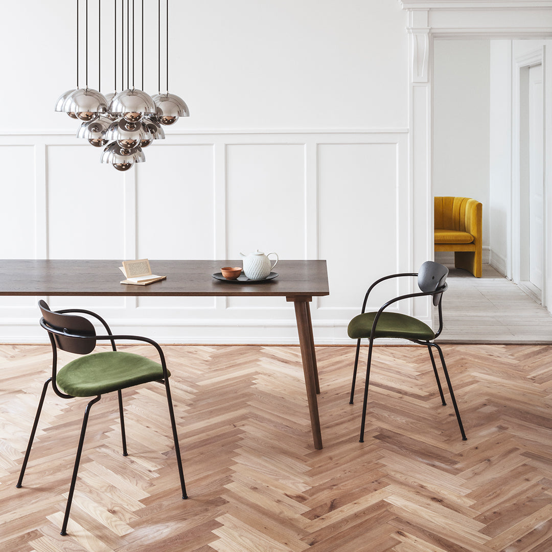 Green upholstered chairs with black frames, natural wood table, and herringbone floor pattern in a bright, modern interior.
