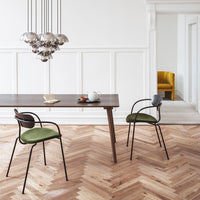 Green upholstered chairs with black frames, natural wood table, and herringbone floor pattern in a bright, modern interior.