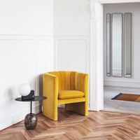 Sleek mustard yellow chair with vertical ribbed upholstery, paired with a modern black side table and light fixture.