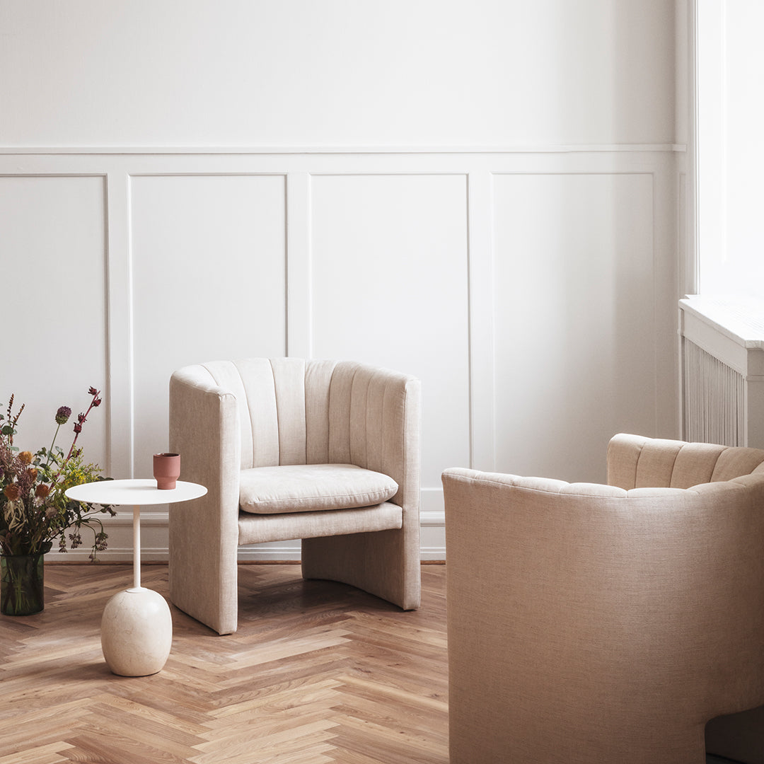 Beige striped armchairs in a light, airy room with wooden herringbone flooring and a simple white side table.