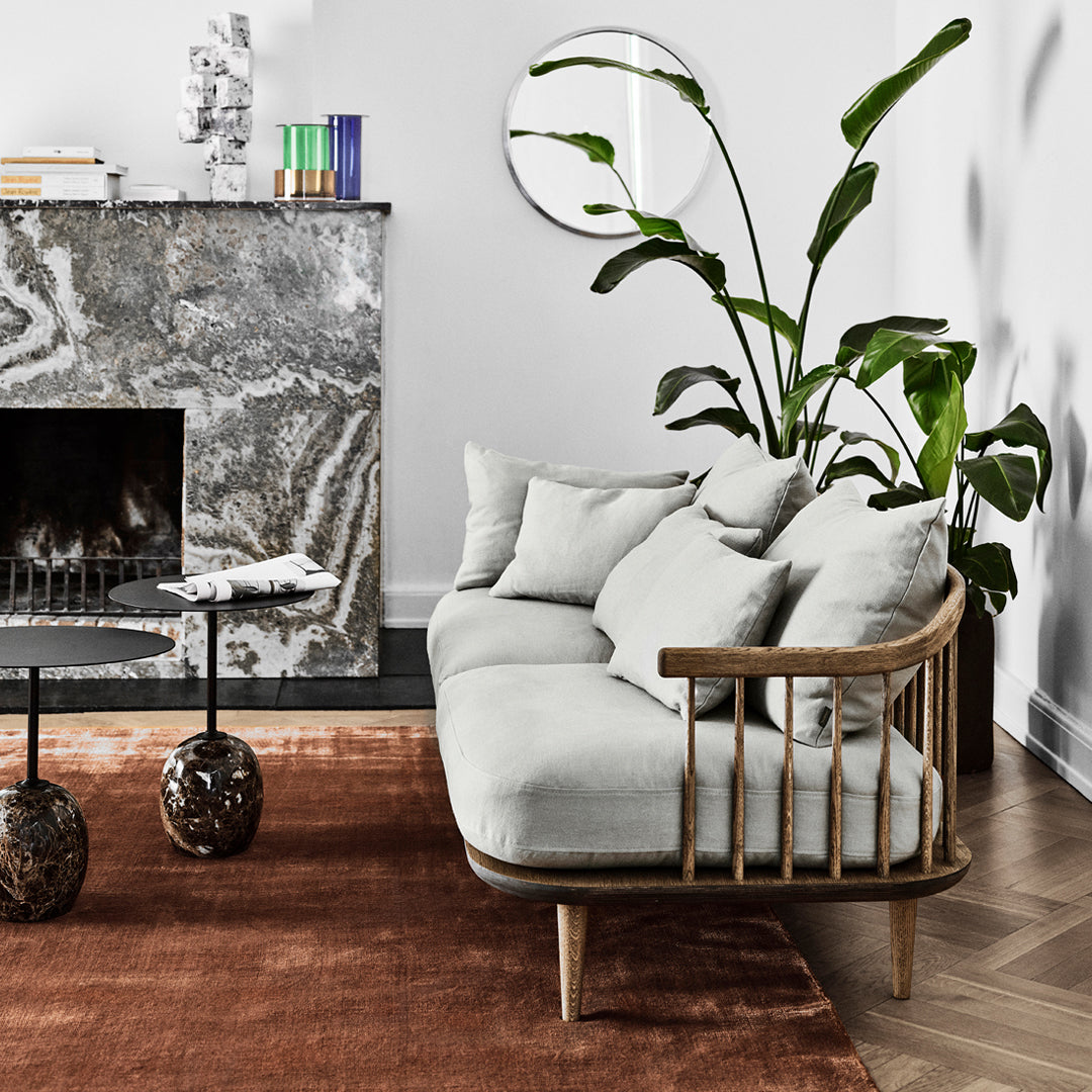 Light grey sofa on a rust-colored rug, elegant marble fireplace, and green leafy plant accents for a modern aesthetic.
