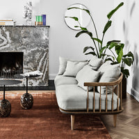 Light grey sofa on a rust-colored rug, elegant marble fireplace, and green leafy plant accents for a modern aesthetic.
