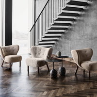 Beige tufted armchairs with dark wooden legs, set against a gray concrete wall and dark herringbone floor.