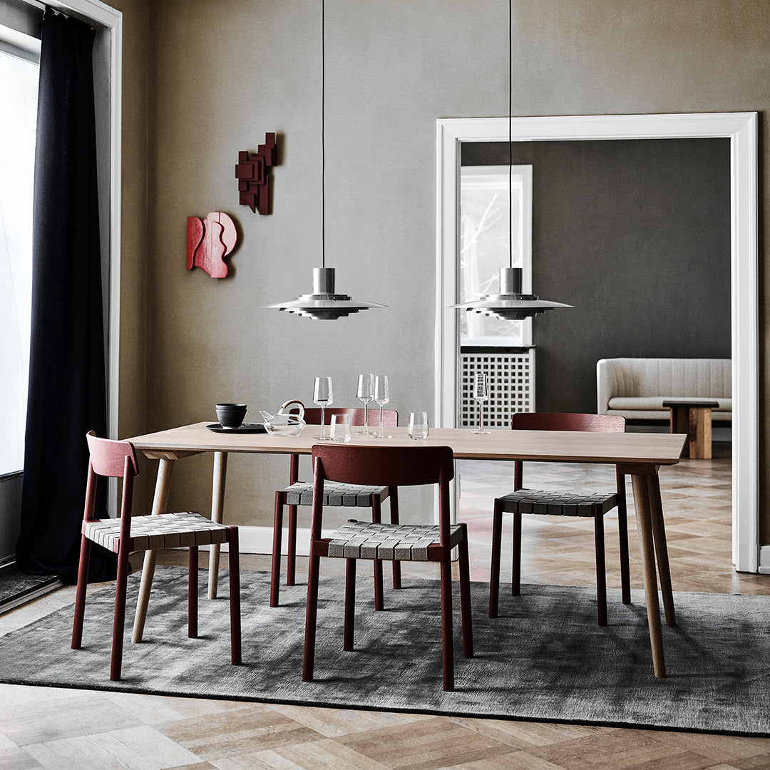 Stylish wood dining table with burgundy and gray chairs, set against a neutral-toned room and patterned rug.
