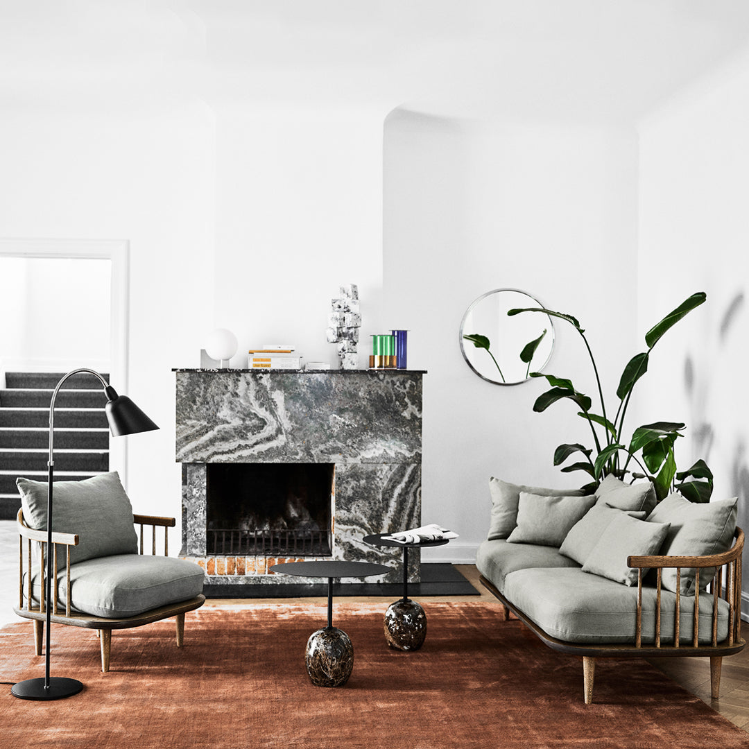 Modern living room featuring a gray sofa, black marble fireplace, and a warm rust-colored rug. Minimalist decor accents.