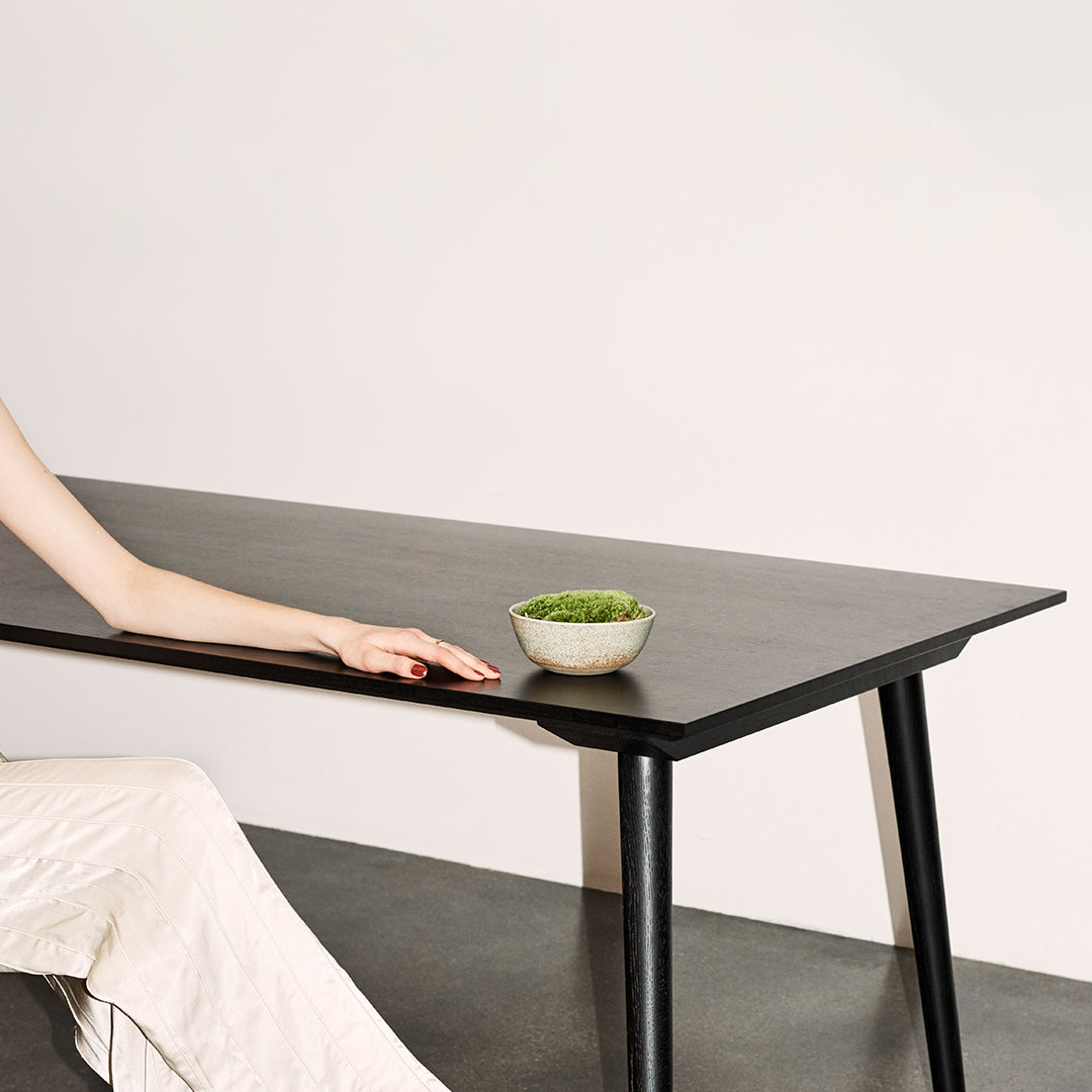 Black dining table with sleek lines, complemented by a minimalist green bowl on a contrasting gray surface.