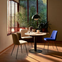 Modern dining set featuring a beige, gray, and blue chair. Simple patterns on a round marble tabletop in a sunlit room.