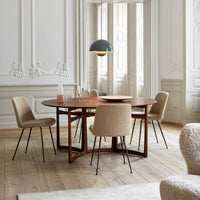Round wooden dining table with beige textured chairs and a muted gray pendant lamp, set in an elegant interior.