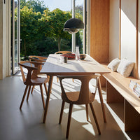 Light wood dining table with light beige chairs, complemented by warm sunlight and green outdoor views.