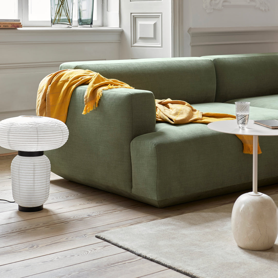 Green modern sofa with a mustard throw, paired with white and beige decor elements on wooden flooring.
