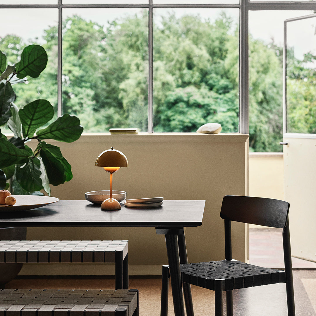 Modern dining setup featuring sleek black furniture, warm wood tones, and lush green plant accents. Natural light enhances the colors.