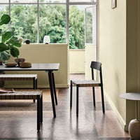 Black chair with woven seat in a bright yellow room, featuring earthy tones and natural textures.