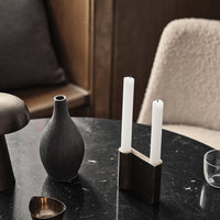 Black and white candle holder with two white candles, gray vase, and various textured decor on a dark tabletop.